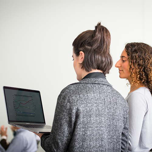 Two people stand together looking at a laptop screen.