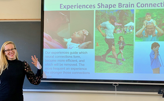 Professor lecturing next to images displayed on classroom screen.