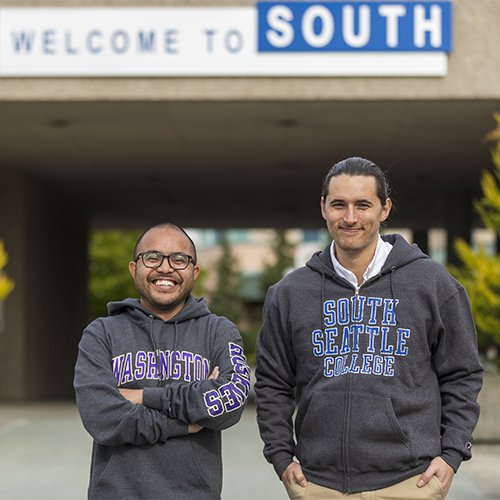 Two smiling men standing shoulder to shoulder in front of building