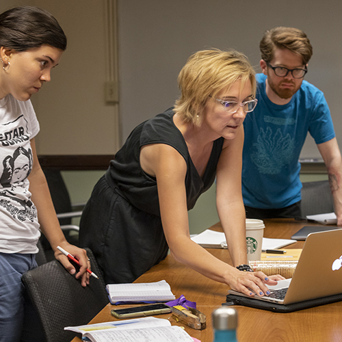 Female teacher on laptop next to two students