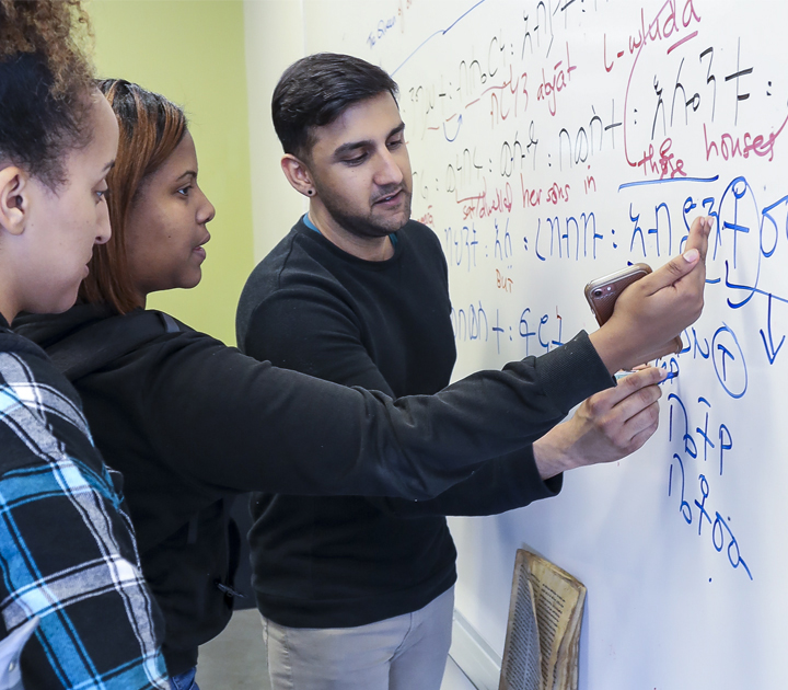 Male teacher gesturing to white board with two students