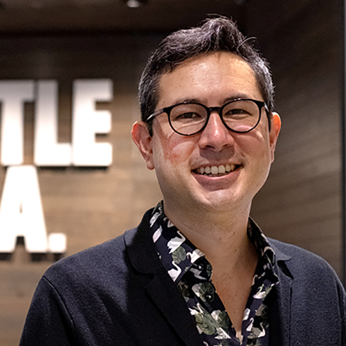 Alex Minami with Seattle Opera sign on the wall behind him