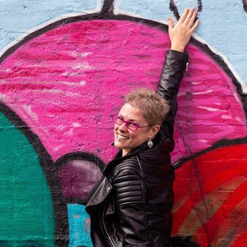 Abby Murray standing in front of colorful mural on exterior wall of building.